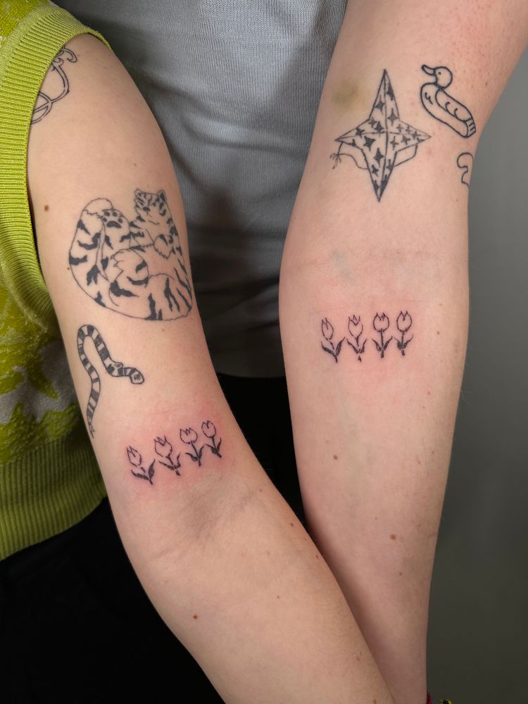 deux bras droits côtes à côtes, le mien à gauche et celui de marie à droite. peaux blanches, plusieurs tatouages sur les deux bras. deux tatouages sont récents, un sur chaque bras, ils représentent quatre tulipes alignées.   