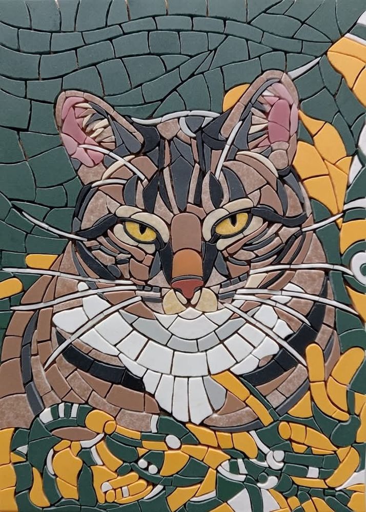 A not yet grouted mosaic of a tabby cat with yellow eyes lying on a "green bay packers" blanket.