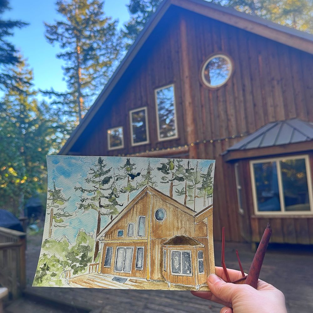 A watercolour painting of woodsy house held in front of the house in the actual painting. 