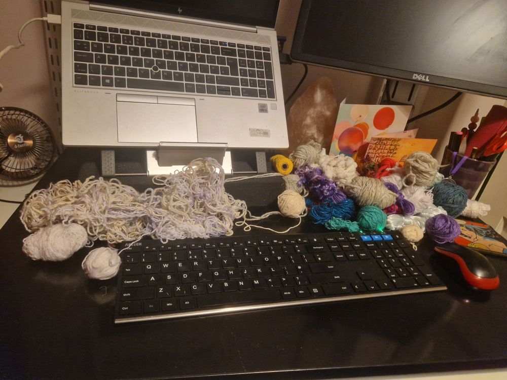 A desk with tangled yarn on one side of the keyboard, and de-tangled balls of yarn on the other. 