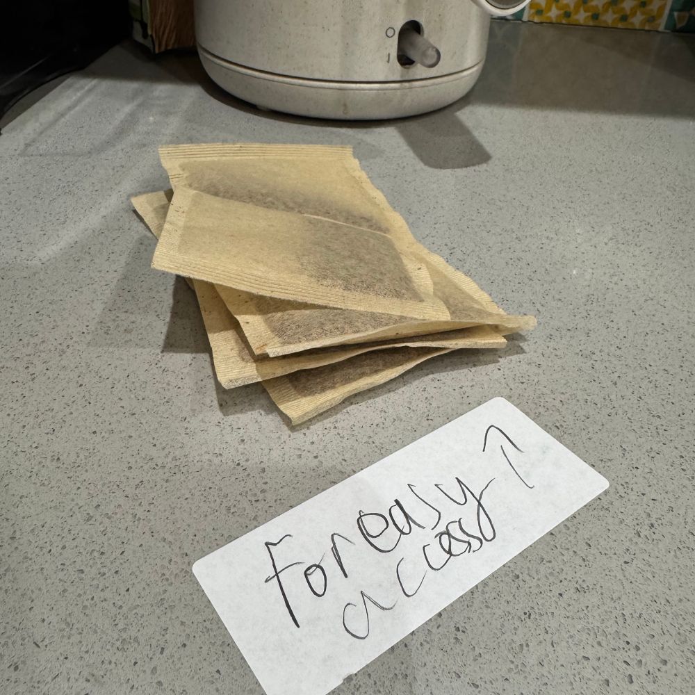 8 loose teabags next to a kettle on a worktop. In the foreground a sticky label with the words “For easy Access” and an arrow pointing to the bags. 