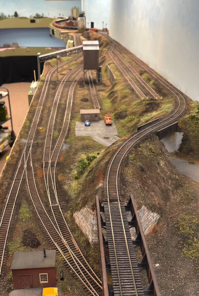 An overhead view of an HO model railroad section with an ore loading area, a small railway shed, an overhead bridge, seven tracks and three switches. Ore spills, rock outcrops and lack of vegetation dominate the scene.