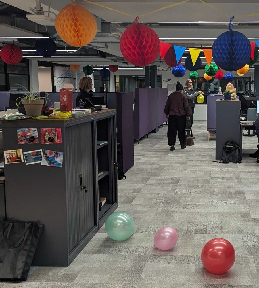 Librarians decorating an office with brightly coloured paper honeycomb pom-poms and balloons. 