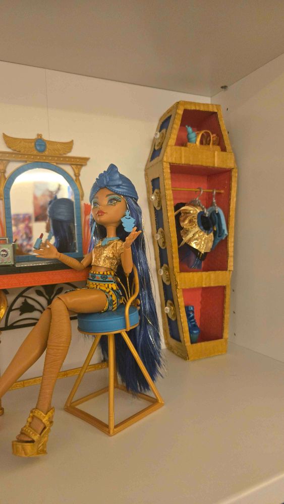 (Monster High) Cleo DeNile sitting at her vanity, a coffin shaped wardrobe behind her.