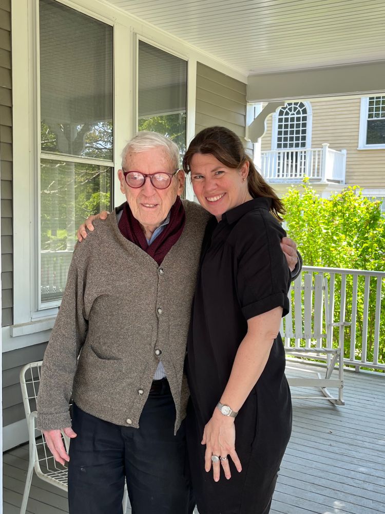 An elderly white man with glasses and a middle aged white woman on a porch in summer
