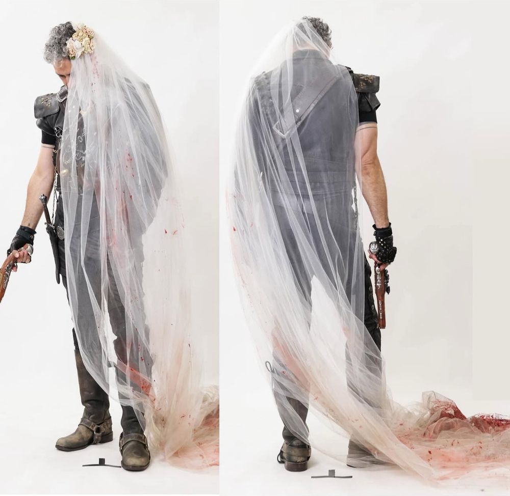 An image of Taika trying on Ed's costume, without wig or tattoos, along with the bloody bridal veil stolen from the wedding raid in 2x01.