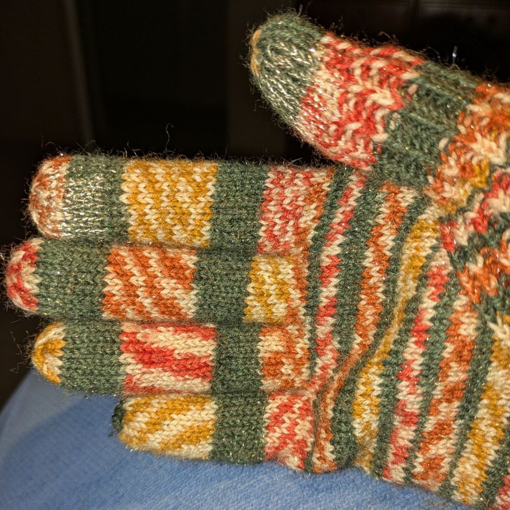The right hand glove. Hand knitted in Christmas self striping yarn. There is a patch of metal thread duplicate stitched on the index finger and thumb. 