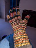 One handknit glove - slightly out of focus. 
Knitted in a Christmas self striping yarn of dark green with candy stripe patterns in between (red and white, yellow and white, rust and white).
