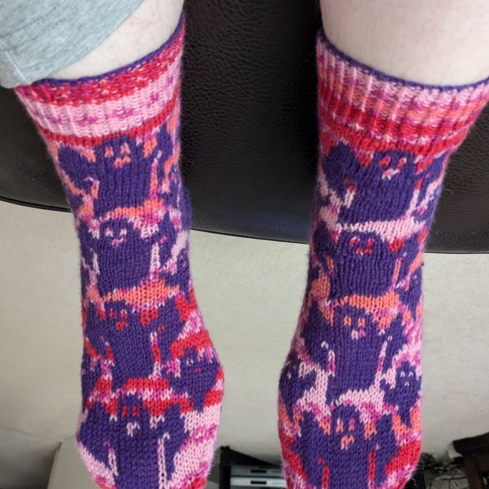 A pair of handknit colourwork socks.
Purple ghosts with a pink self striping background.
This view is of the leg and top of the feet. 