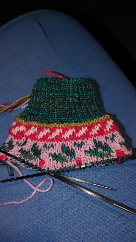 Handknit sock with green cuff, candy cane pattern block and then holly leaf pattern block with red berries. 