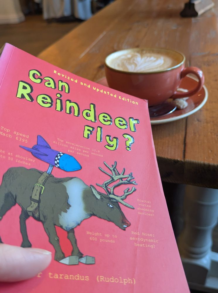 A cup of coffee is on a pub table. I'm holding the book Can Reindeer Fly? The Science of Christmas. 