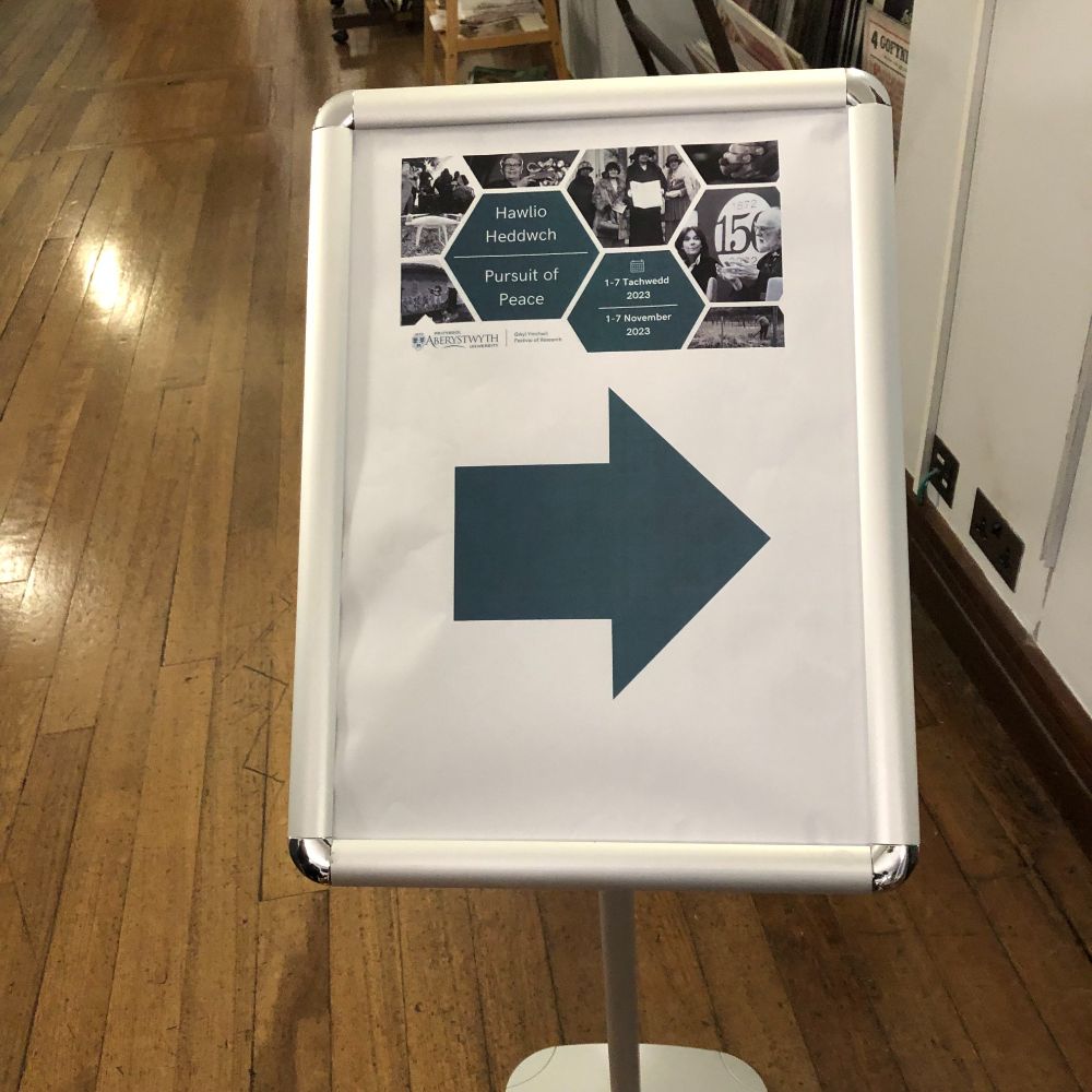 Photograph of a direction sign, with the logo of the Aberystwyth University festival of research and a large arrow