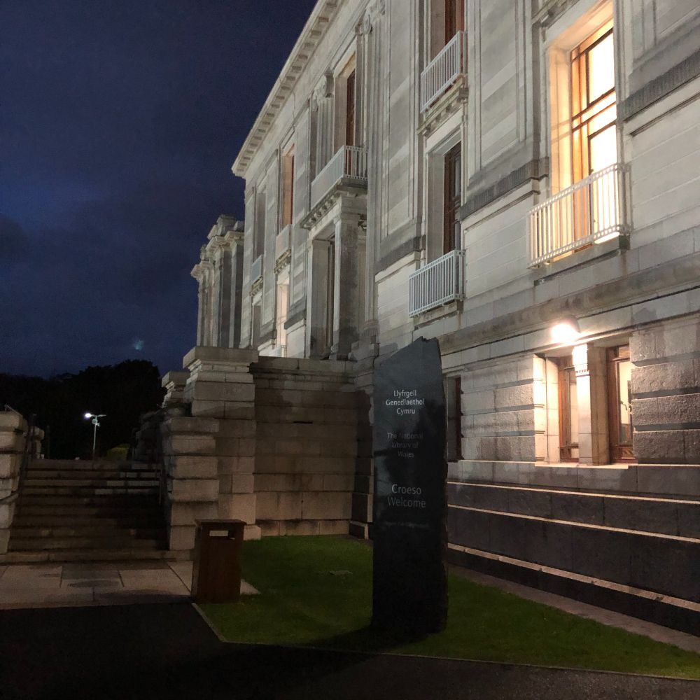 Photograph of a neoclassical white building lit up at night: the National Library of Wales in Aberystwyth