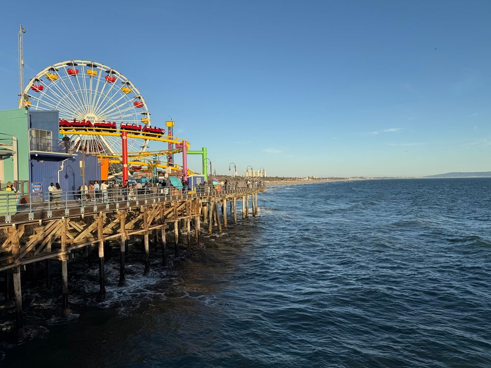 The Ferris wheel and rollercoaster of Santa Monica pier with the ocean rolling up again the wood suppor