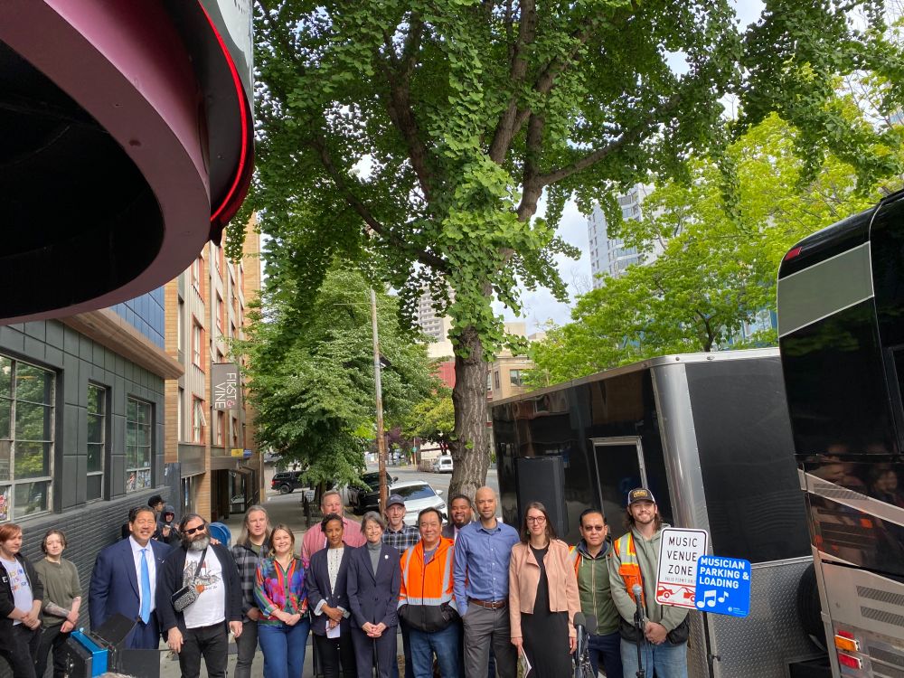 Council President Nelson and Mayor Harrell with members of Seattle's music industry standing behind a sign that reads "Music Venue Zone, Musician Parking & Loading" 