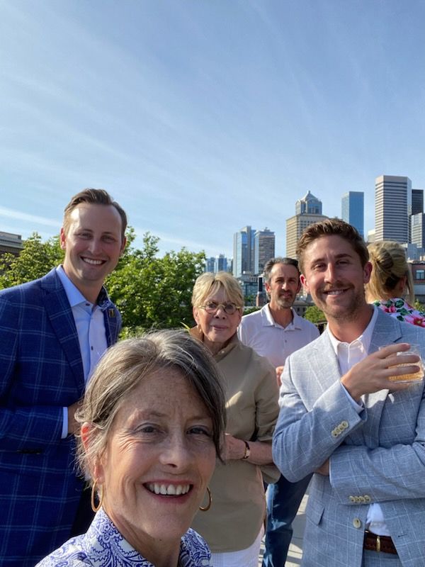 Council President Sara Nelson (front) with Jack Ross (left), Development Manager for Urban Villages, Midge McCauley (center) from Downtown Works, and Henry Watson (right), Development Manager for Urban Villages. Standing in front of the Seattle Skyline at a rooftop bar. 