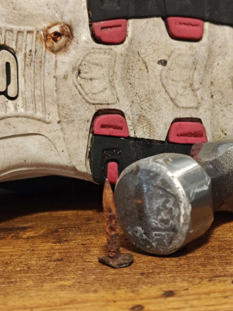 Whelp, that could have gone poorly! An inch long rusty nail sits in front of a sneaker and the head of a hammer. The nail appears rusty and about an inch long
