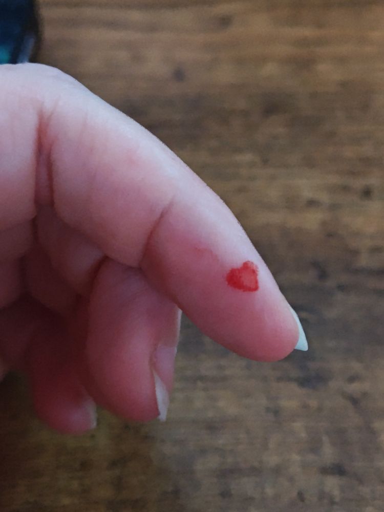A squished blood droplet on a finger, now hollow in the center and turned vaguely heart shaped from the tip of the test stick