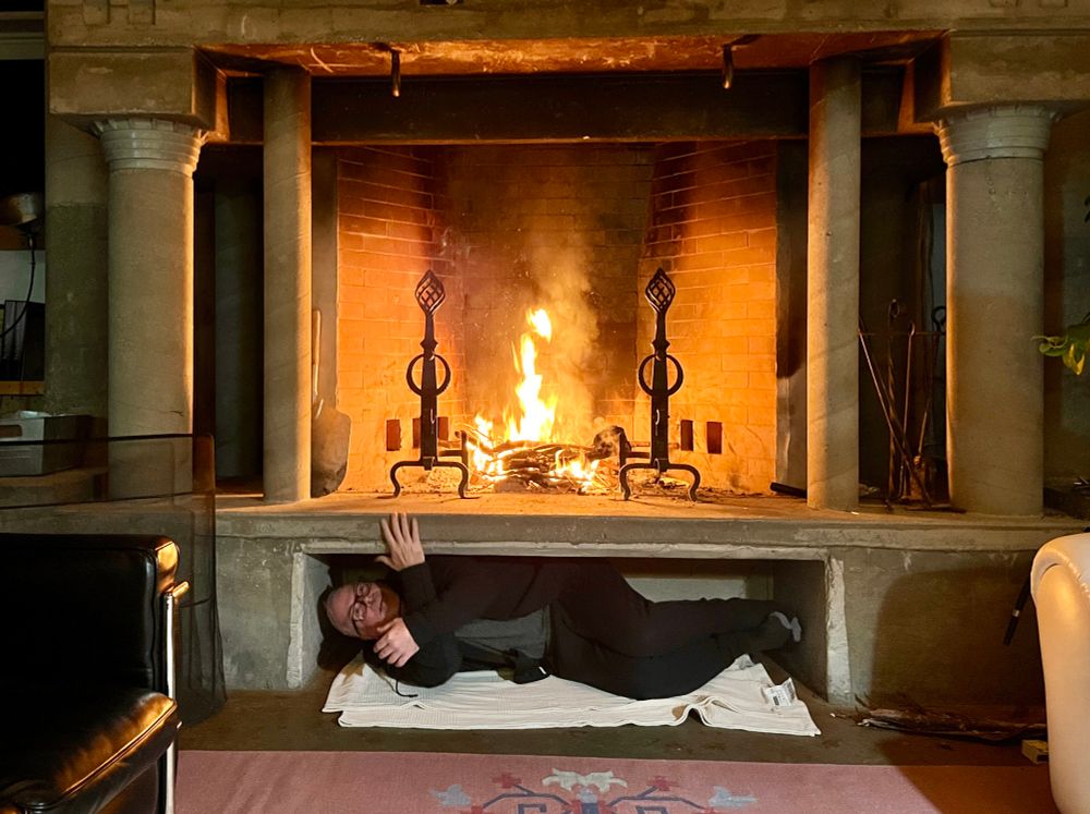 jeff horizontal in alcove under the fire place with the fire raging