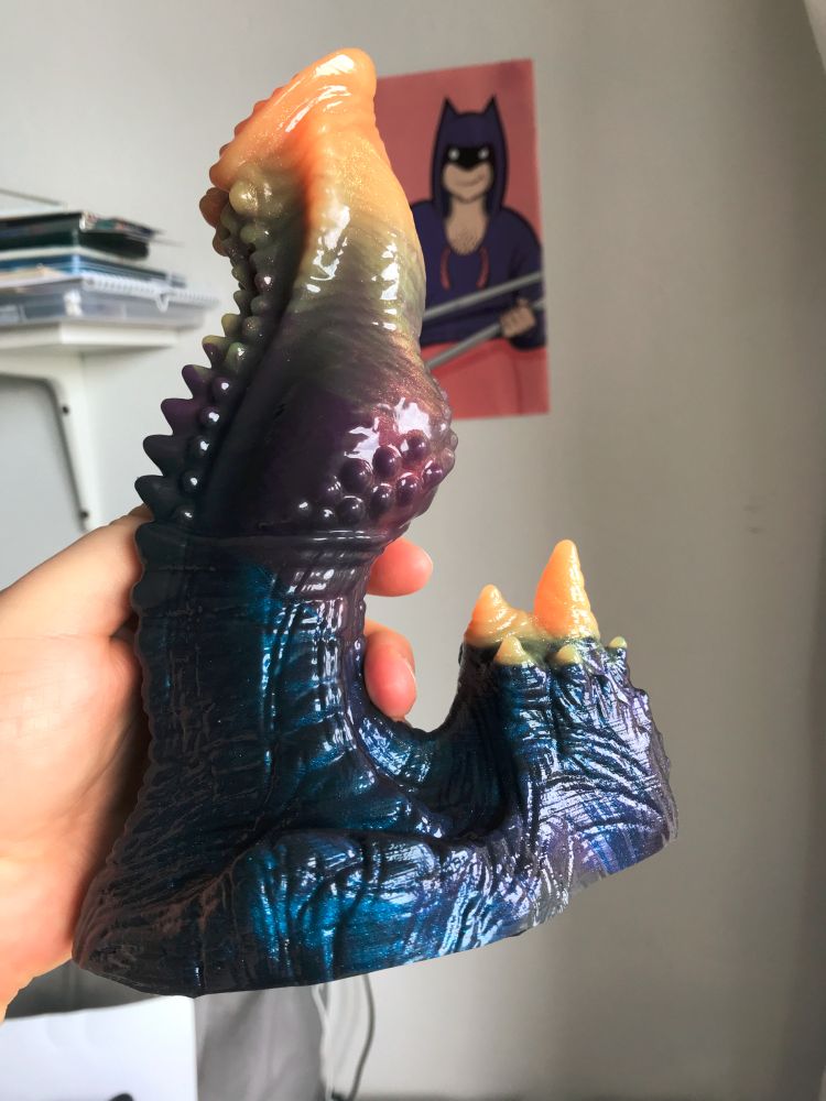 DTE Volente held in my hand. it's a fantasy dildo with rows of nubby spikes running down its back, a flared head and a knot. 
