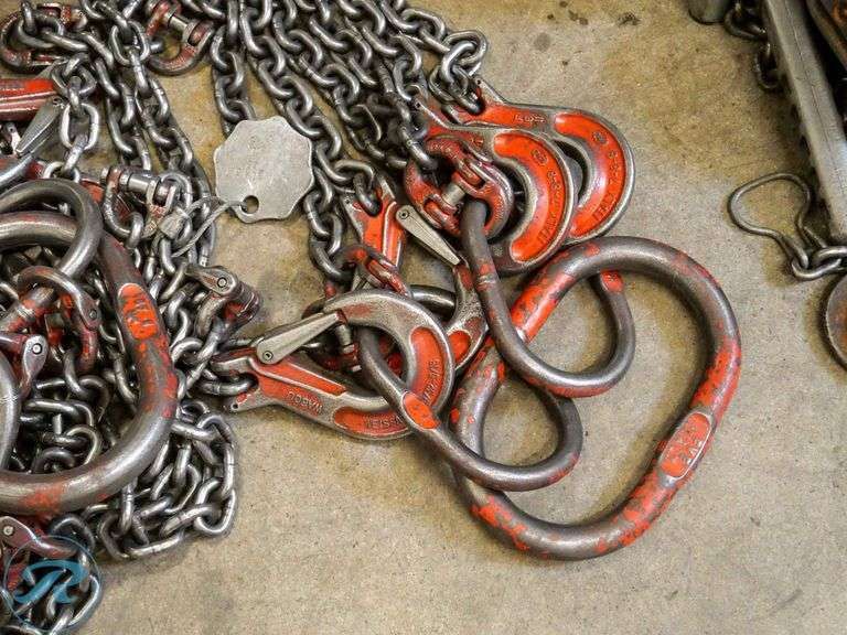 heavy rigging chains, hooks and rings lying on a concrete floor. they've definitely seen hard use, the paint is chipped off in places, but they're well maintained and not rusty. 