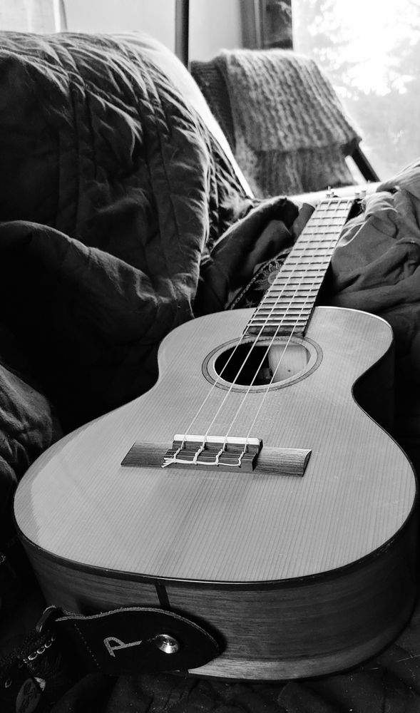 A black and white photo of a ukulele laying on material. A chair with a knitted shawl is in the background