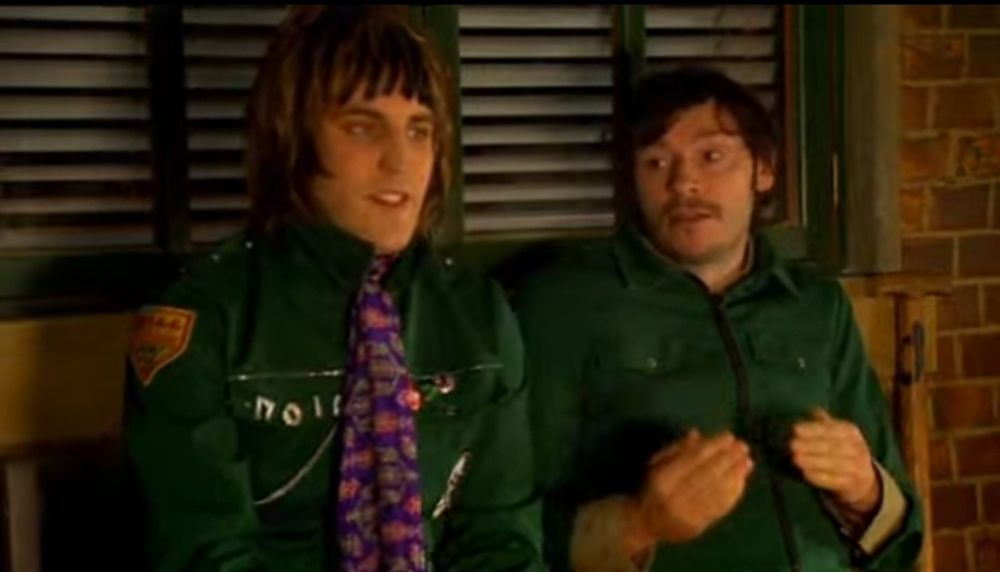 Noel Fielding in a green jacket with a purple and pink flowing tie and Julian Barratt, also in a green jacket, from The Mighty Boosh.