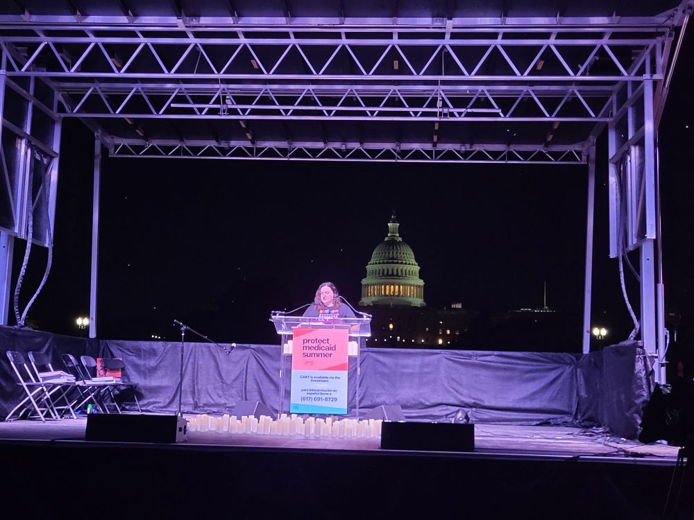 Photo of Nicole speaking on the Protect Medicaid Summer stage at 5am on the National Mall, with the Capitol building behind her. 
