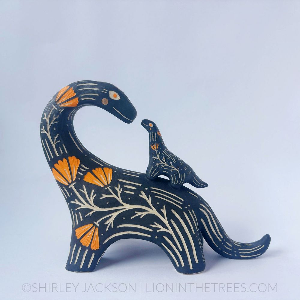 A sgraffito ceramic sculpture done with black and orange underglazes, gold gilding, and my signature California poppies motif. The sculpture is that of a sauropod dinosaur that has a smaller sauropod on it's back. The larger sauropod's neck is craned towards the smaller one as though they're about to boop noses.