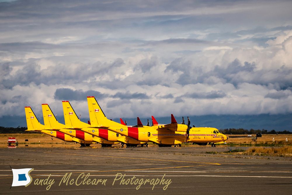 Lineup of 4 search and rescue aircraft at an airfield with a low cloud deck in the background. 