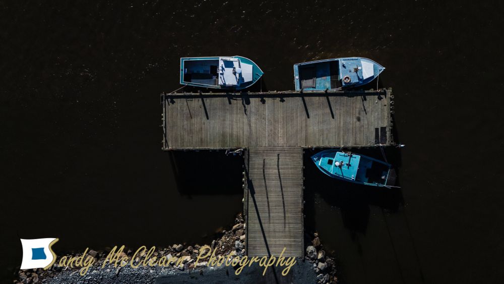 Three fishing boats at a T-shaped wharf as seen from above. 