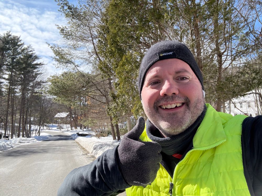 Jon Masters pauses to take a selfie during an outdoor winter run. He is wearing a bright greenish yellow safety vest.