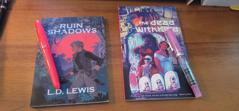Novella "A Ruin of Shadows" paired with a neon pink esterbrook fountain pen

Novellas "The Dead Withheld" paired with a TWSBI Eco fountain pen in Glow Purple