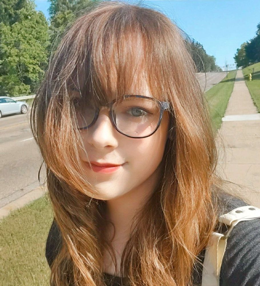 A close-up of Erika (me) walking outside on a sidewalk next to a 5-lane road during a bright and sunny day