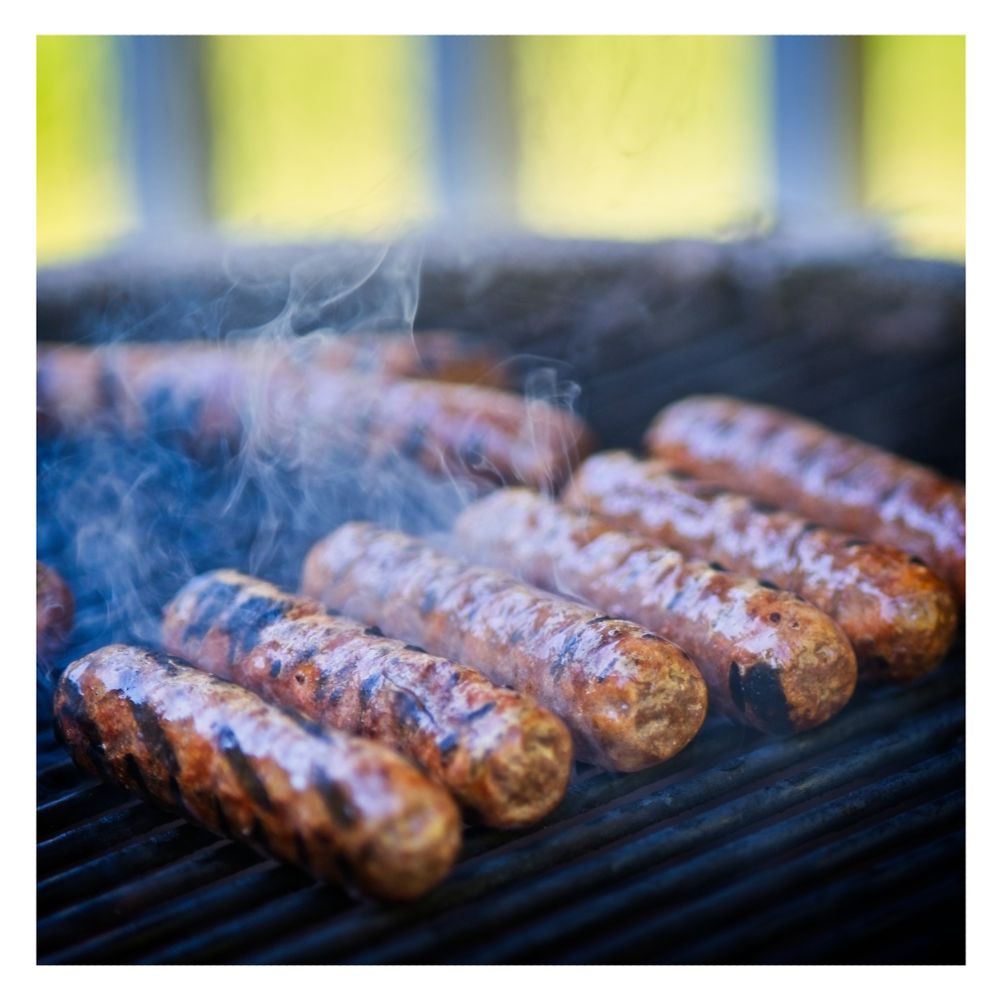Sausages cooking on a grille with smoke rising