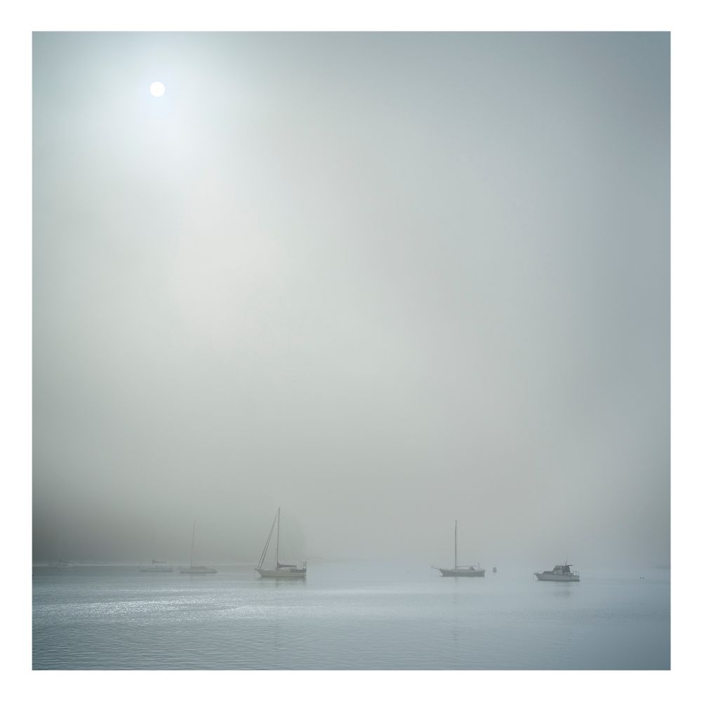 Boats in the fog with a white sun