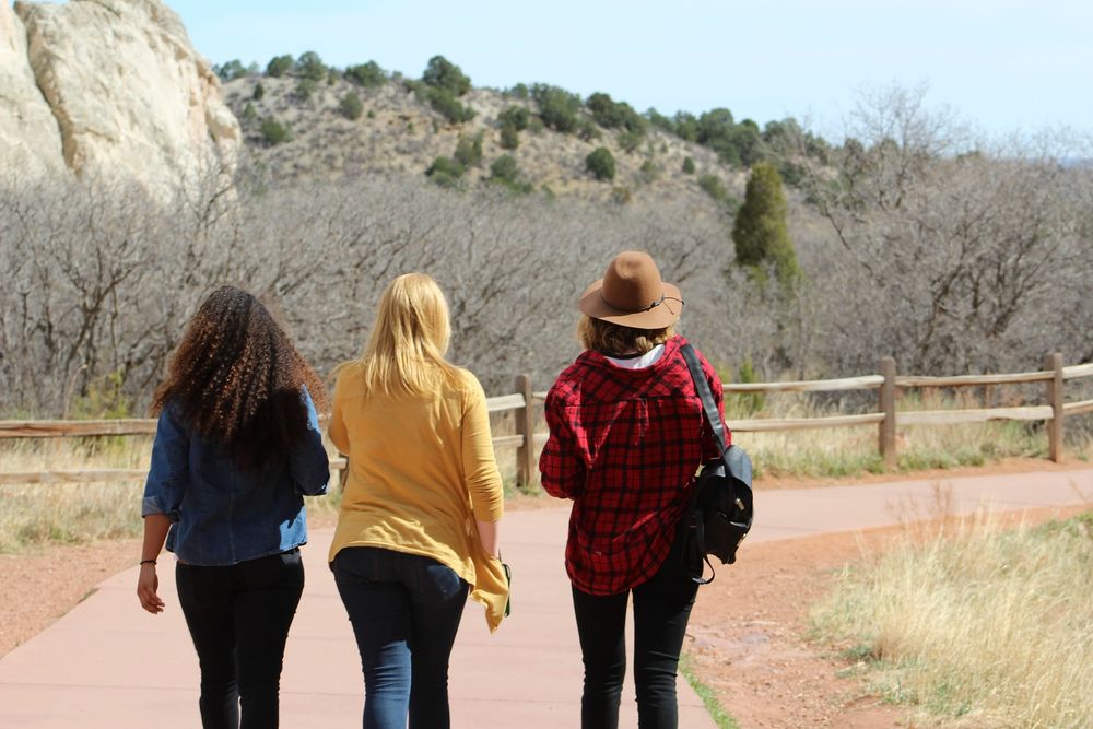 Three women walking together along a trail on a sunny day.