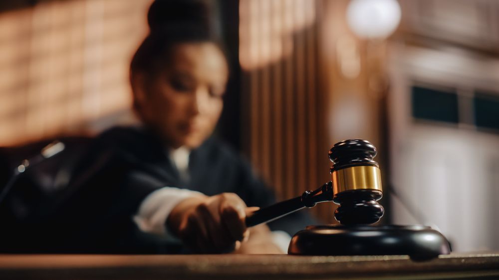 A dark-skinned woman using a gavel in a courtroom.