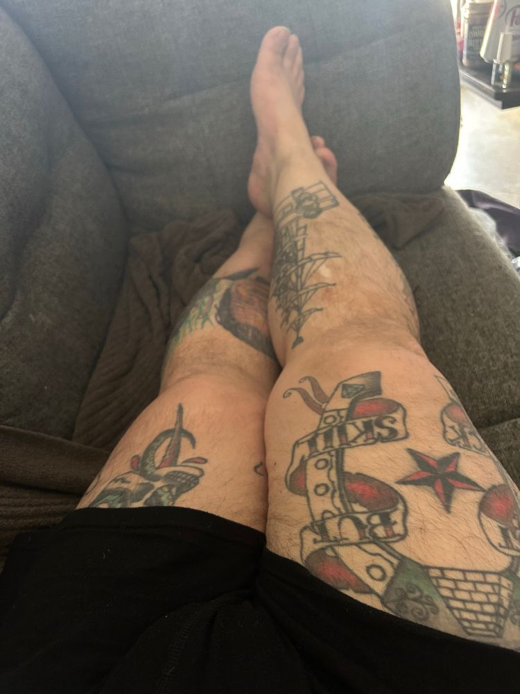 Photo of a set of tattooed legs crossed at the ankles laying on a grey couch 