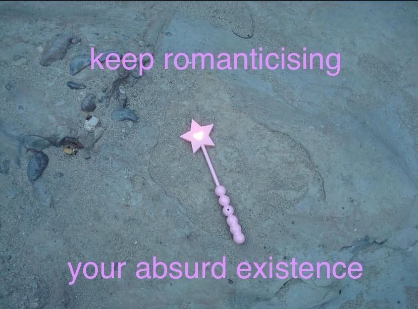 a pink star wand on the sand and pink text that reads: “keep romanticizing your absurd existence”