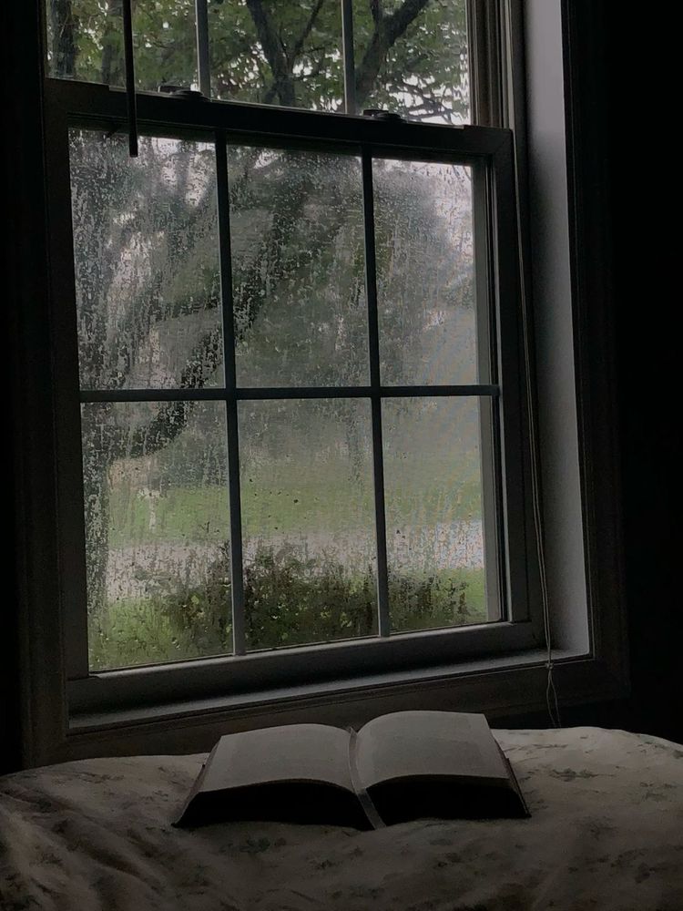 an open book on a bed by the window on a rainy day