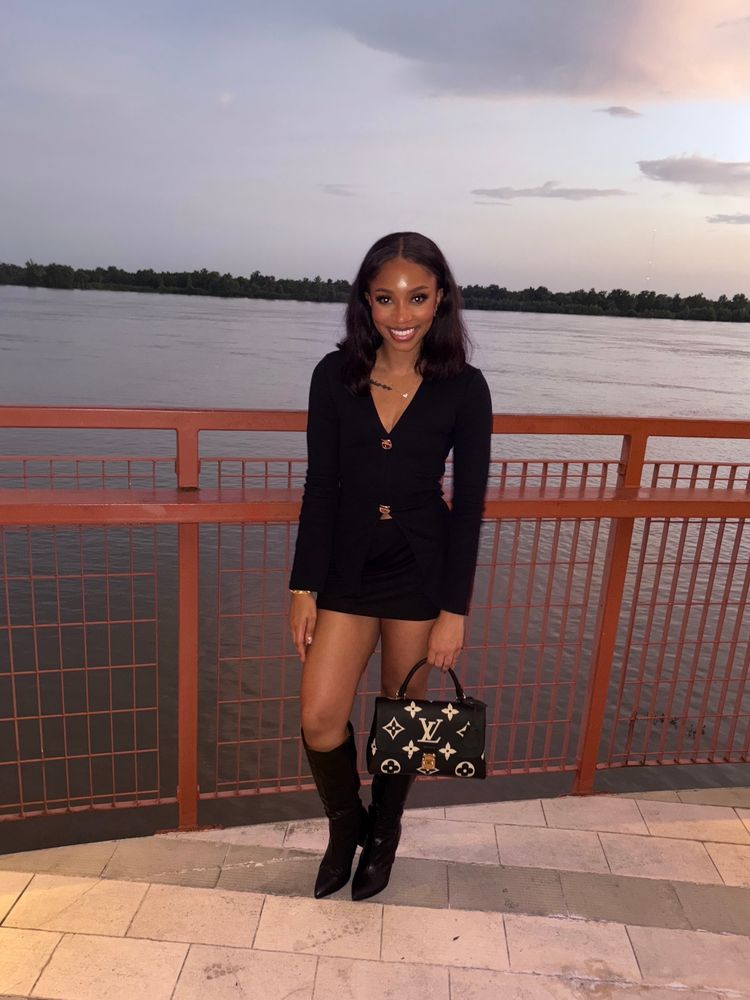 Smiling girl serving face while wearing all black and standing in front of a river 