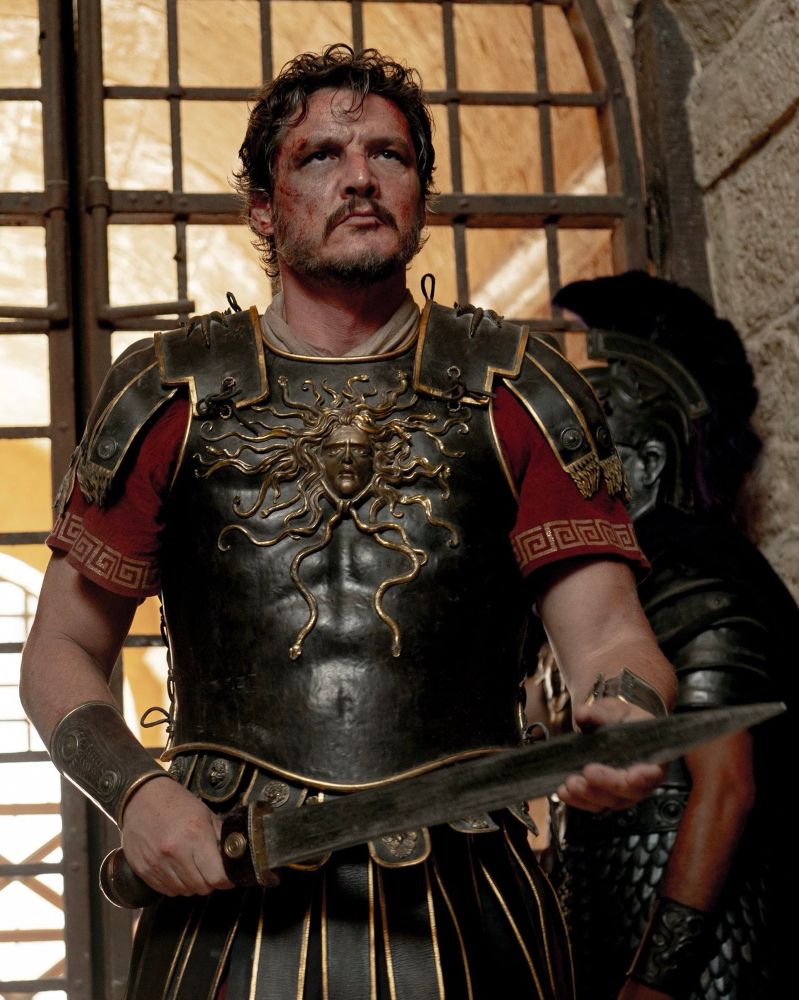Pedro Pascal in his Gladiator role as Marcus Acacius in Roman armor holding a short sword in one hand and the blade resting in his other hand, looking quite pissed off  