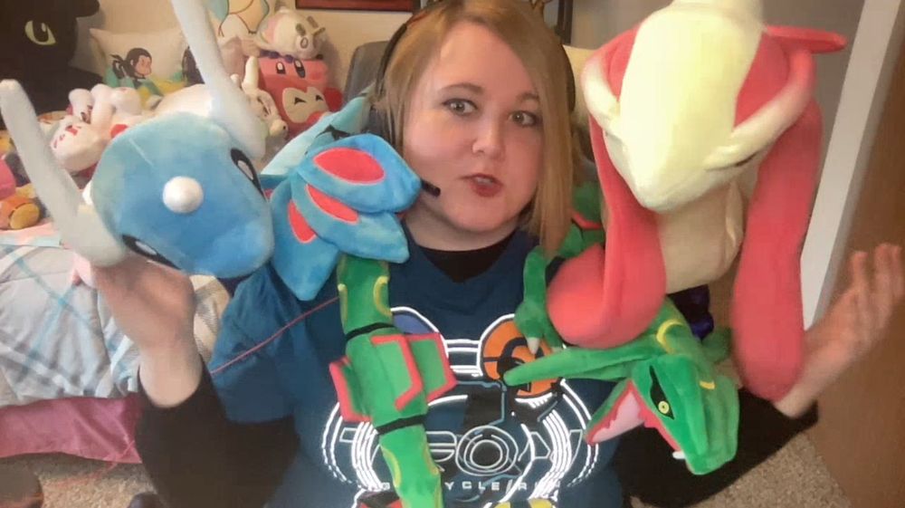 Picture of me with large plushes of the Pokémon Rayquaza, Dragonair, and Milotic draped over my shoulders.