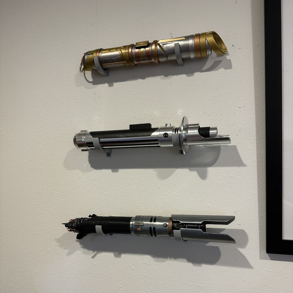 3 lightsaber hits - each sitting on mounting grey brackets attached to a white wall.