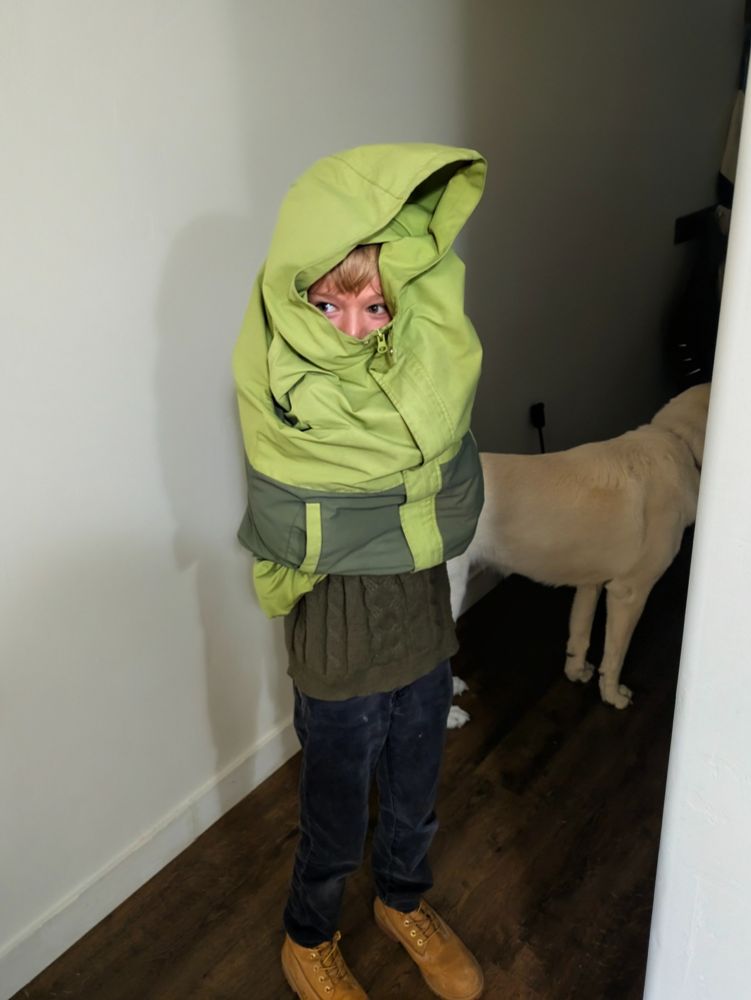 Boy wrapped up in a green coat, his head peeking out 