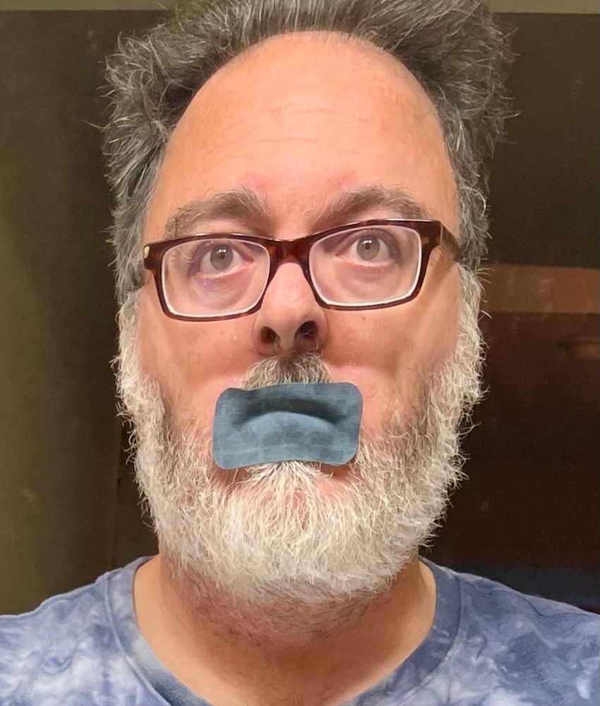 face of an aging man with tape on his mouth.