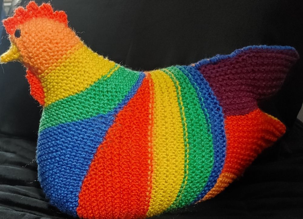 A side view of a hand knit chicken in a rainbow striping yarn.