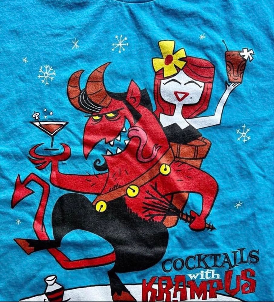 Blue t-shirt fabric with "Cocktails with Krampus" written below a cartoon of a red goat-devel with a switch and a cocktail in his hand. In the basket on his back, a happy woman with a flower in her hair and a tropical cocktail.