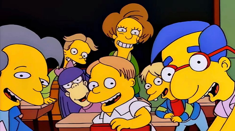 Simpsons screenshot: first person view of Bart, a bunch of kids in a classroom and their teacher all excitedly looking back at him saying “Say the line, Bart!”